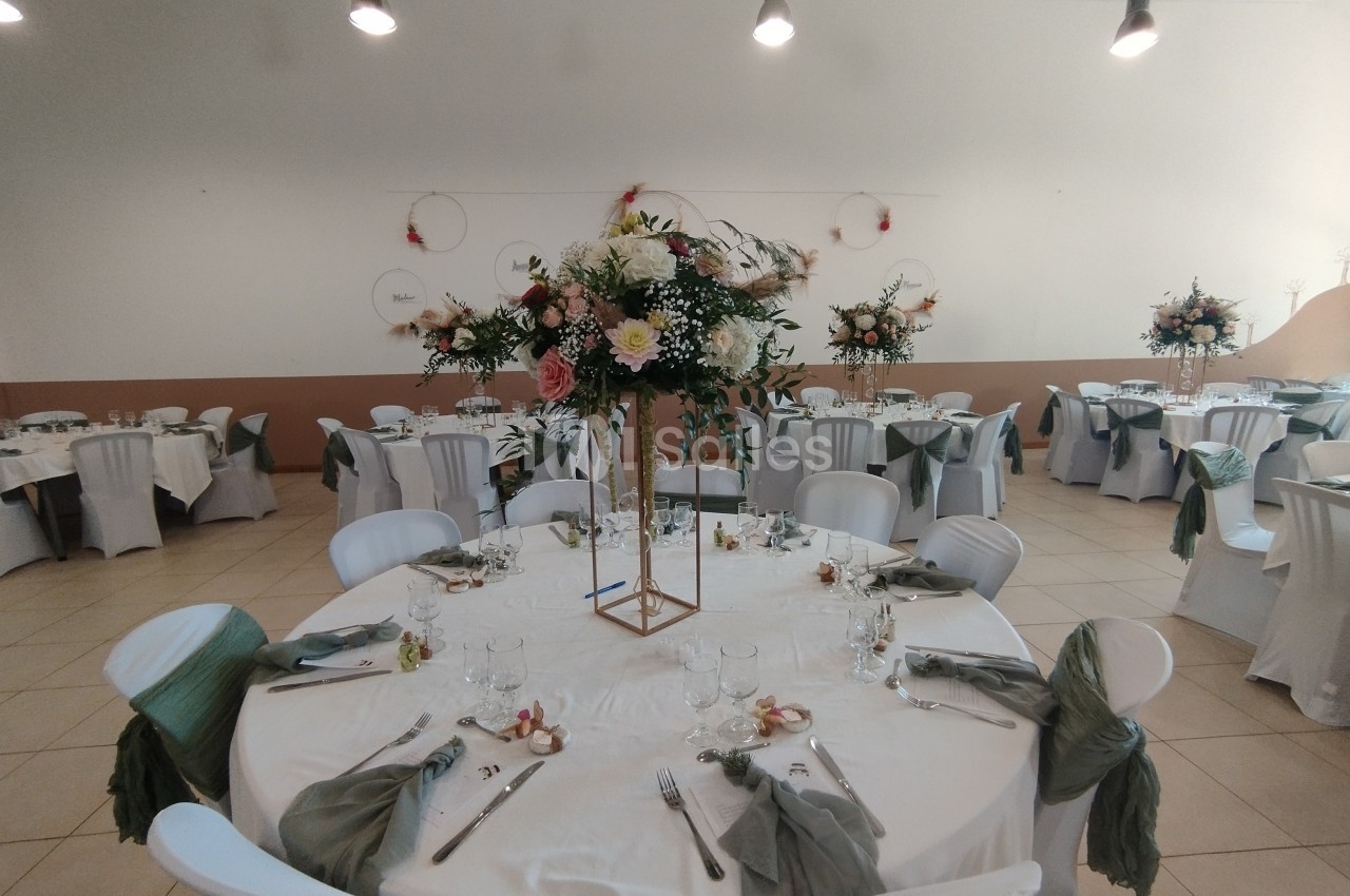 Salle de réception décorée avec des tables rondes, nappes blanches, chaises habillées et centres de table floraux.