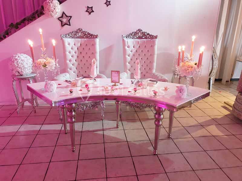 Table de réception décorée avec chandeliers, pétales de rose et deux fauteuils capitonnés blancs dans un cadre élégant.
