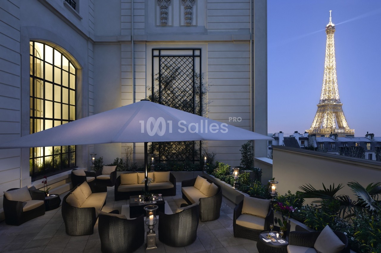 Terrasse élégante avec mobilier de jardin, éclairée le soir, offrant une vue sur la tour Eiffel illuminée.
