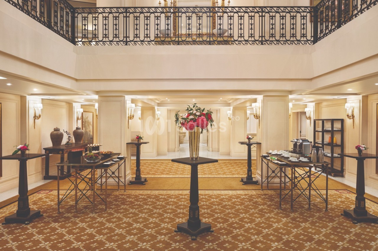 Salle élégante avec un buffet disposé sur des tables hautes, décorée de fleurs et éclairée par des appliques murales.