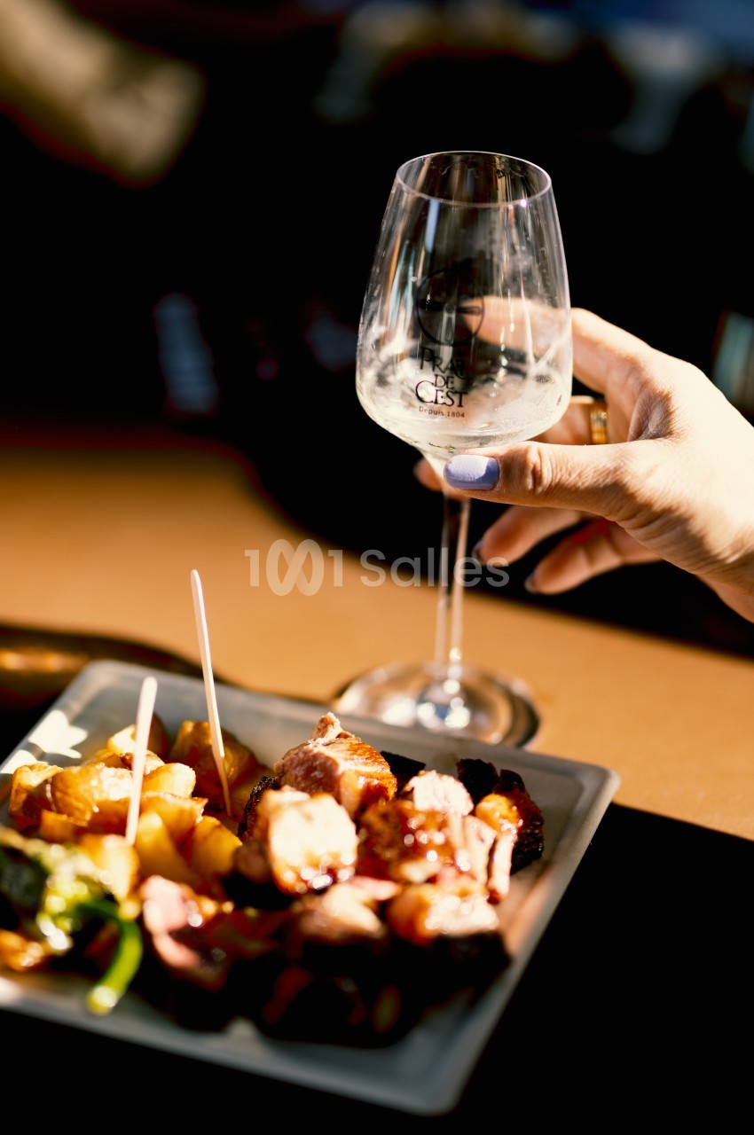 Une main tenant un verre de vin blanc près d'une assiette de viande grillée et de légumes sur une table.