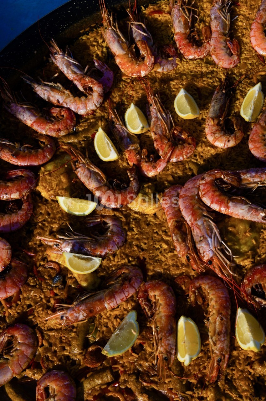 Paella garnie de crevettes roses grillées, quartiers de citron et riz doré.