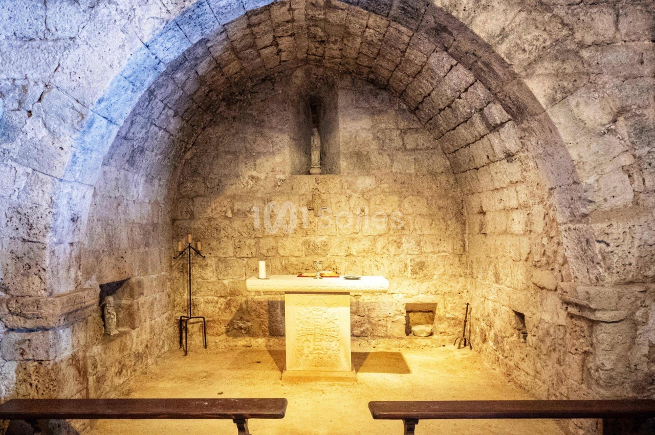 Intérieur d'une petite chapelle en pierre avec un autel central, des bancs en bois et une statue dans une alcôve.