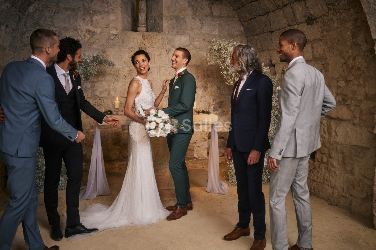 Un couple de mariés souriants entouré de leurs témoins dans une salle en pierre au décor sobre et élégant.