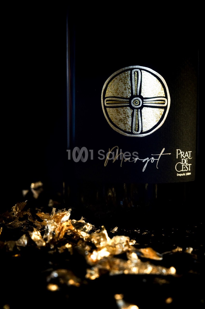 Bouteille de vin sombre avec un logo doré circulaire et des éclats dorés dispersés au premier plan.