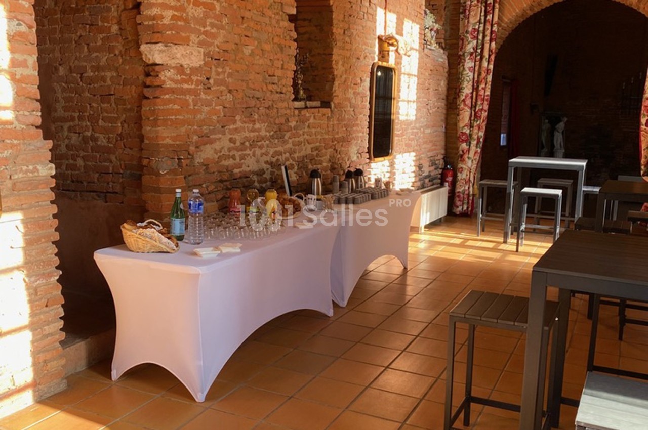 Table de buffet dressée avec boissons et verres dans une salle en briques avec lumière naturelle.