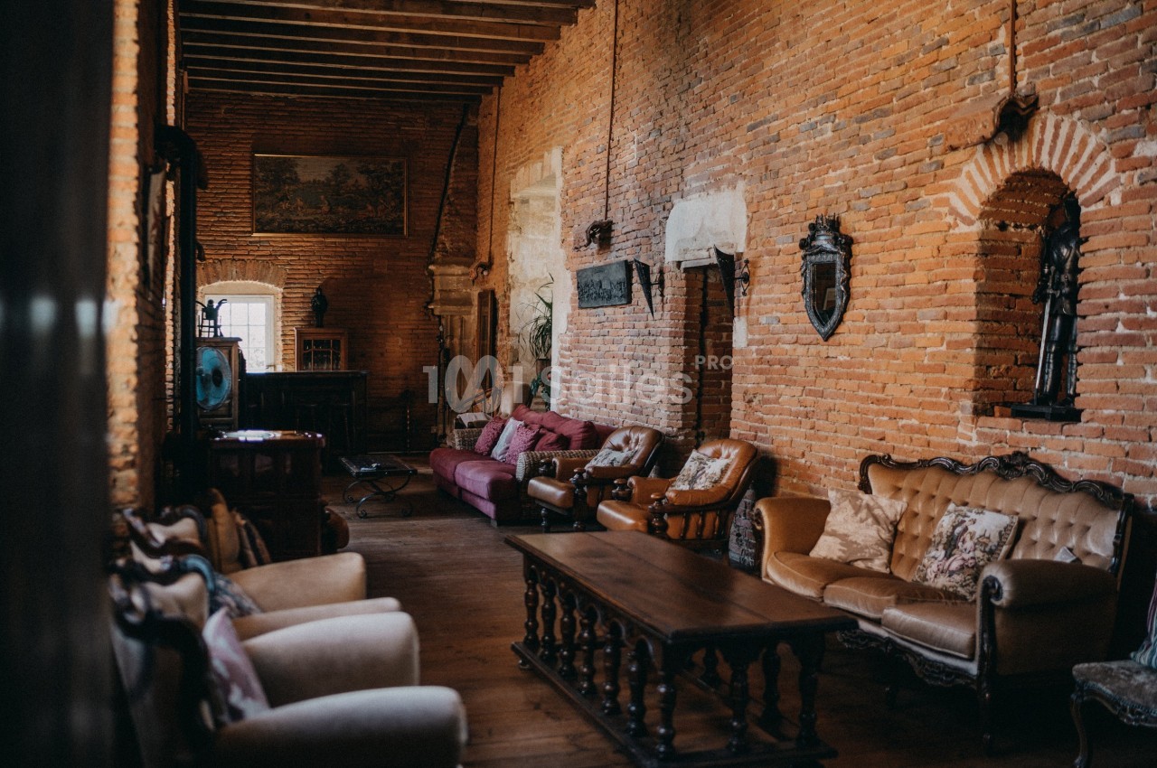 Salon rustique avec murs en briques apparentes, mobilier ancien en bois et canapés disposés autour d'une table basse.