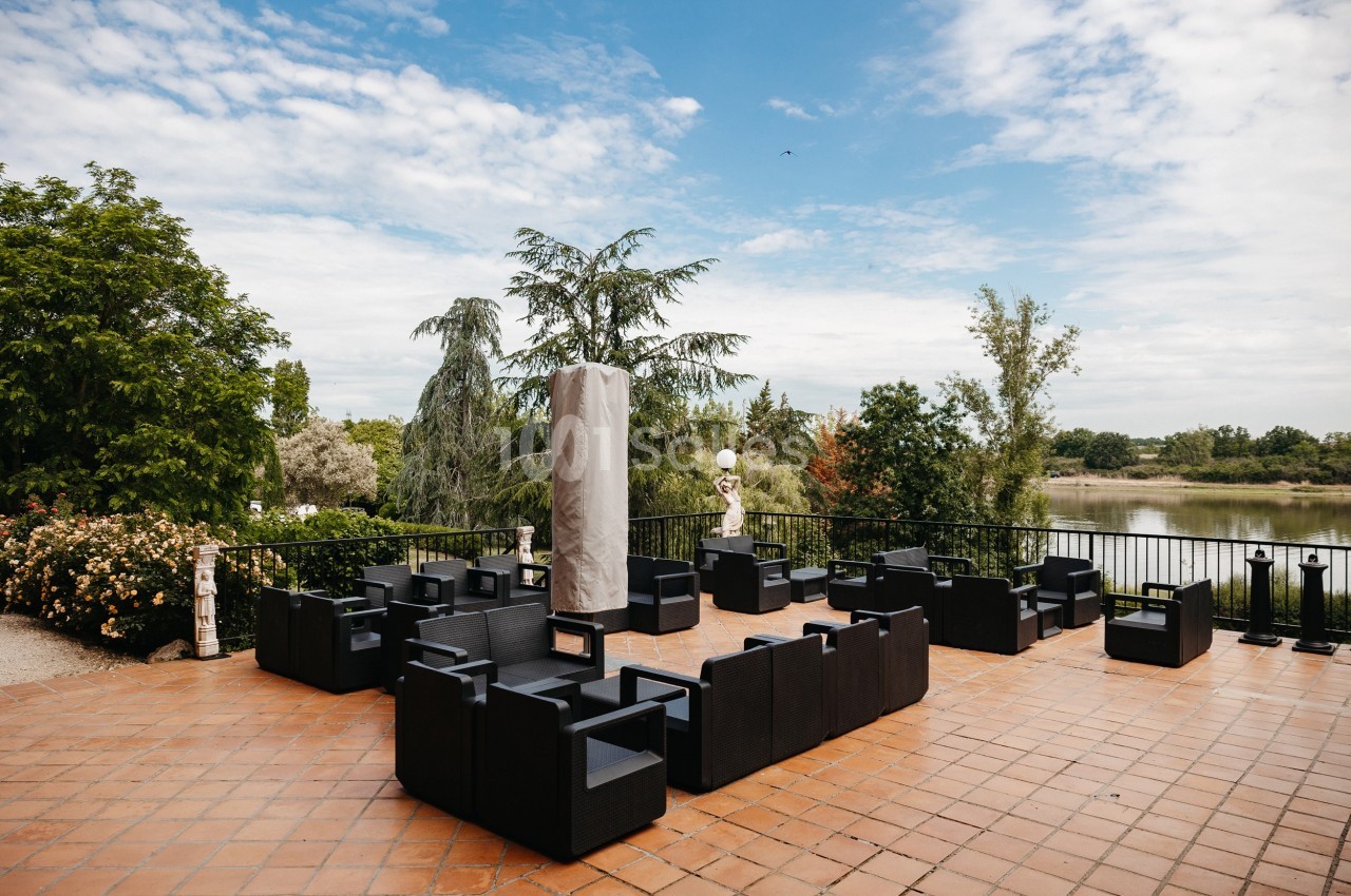 Terrasse en briques avec des fauteuils noirs, entourée de végétation et offrant une vue sur un plan d'eau.