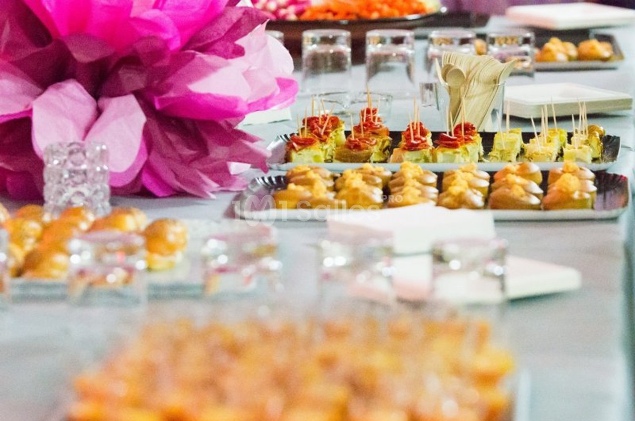 Plateau de bouchées apéritives variées disposées sur une table avec des décorations roses en arrière-plan.