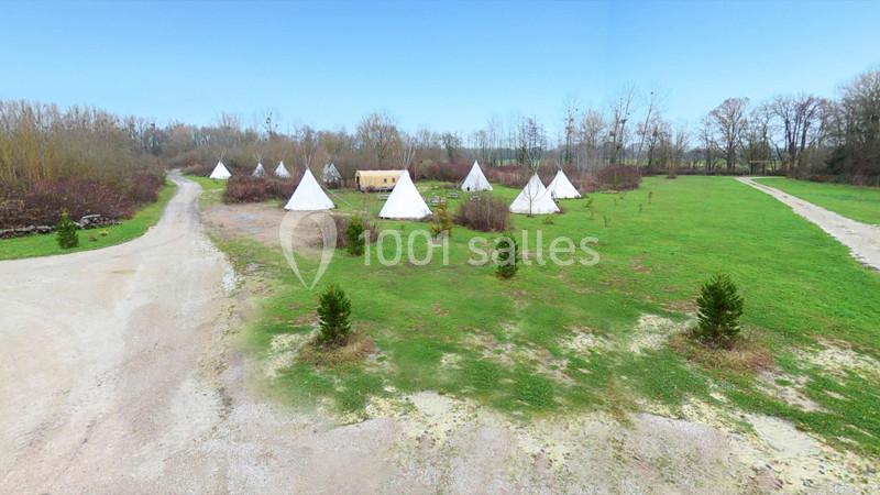 Vue d'un terrain avec plusieurs tipis blancs entourés de verdure et de chemins en gravier.