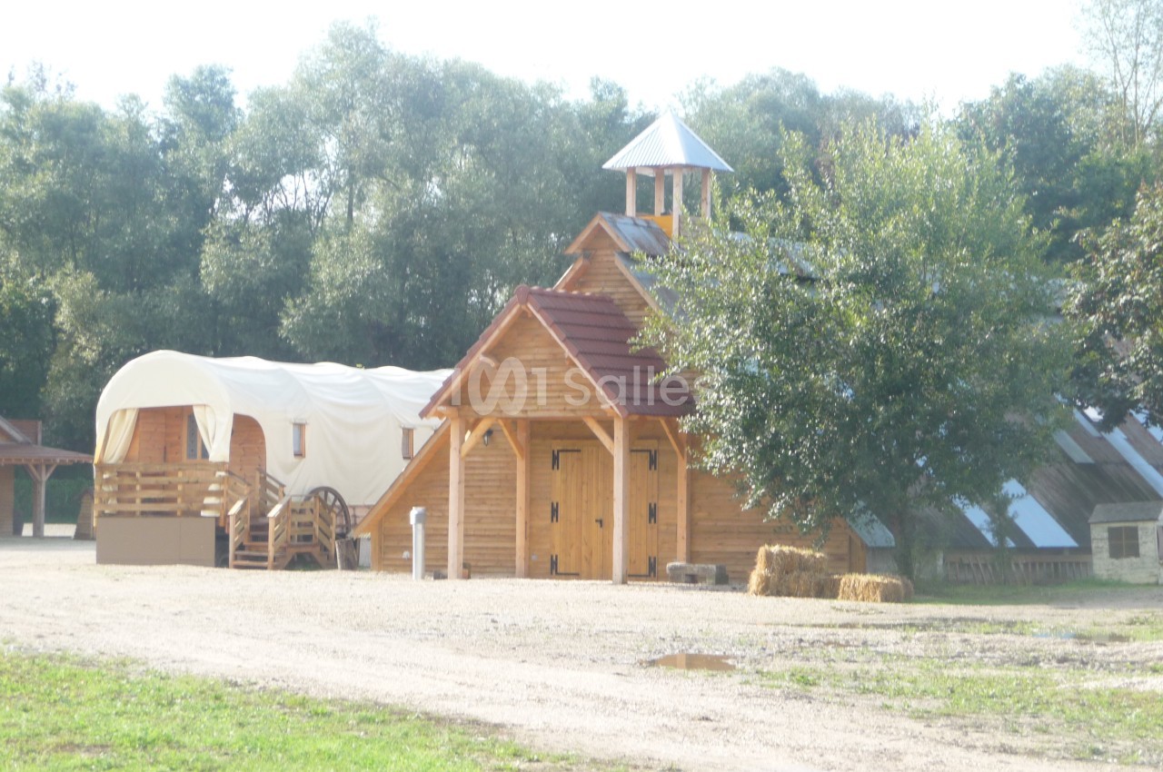 Bâtiments en bois de style western avec une roulotte et un arbre, entourés de verdure.