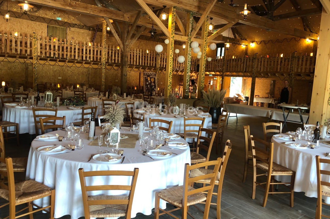 Salle de réception en bois décorée avec des tables rondes dressées pour un événement festif.