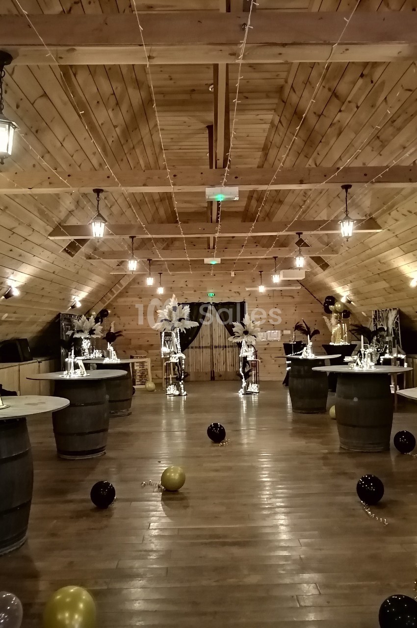 Salle en bois décorée pour un événement, avec tables sur tonneaux, ballons au sol et éclairage suspendu.
