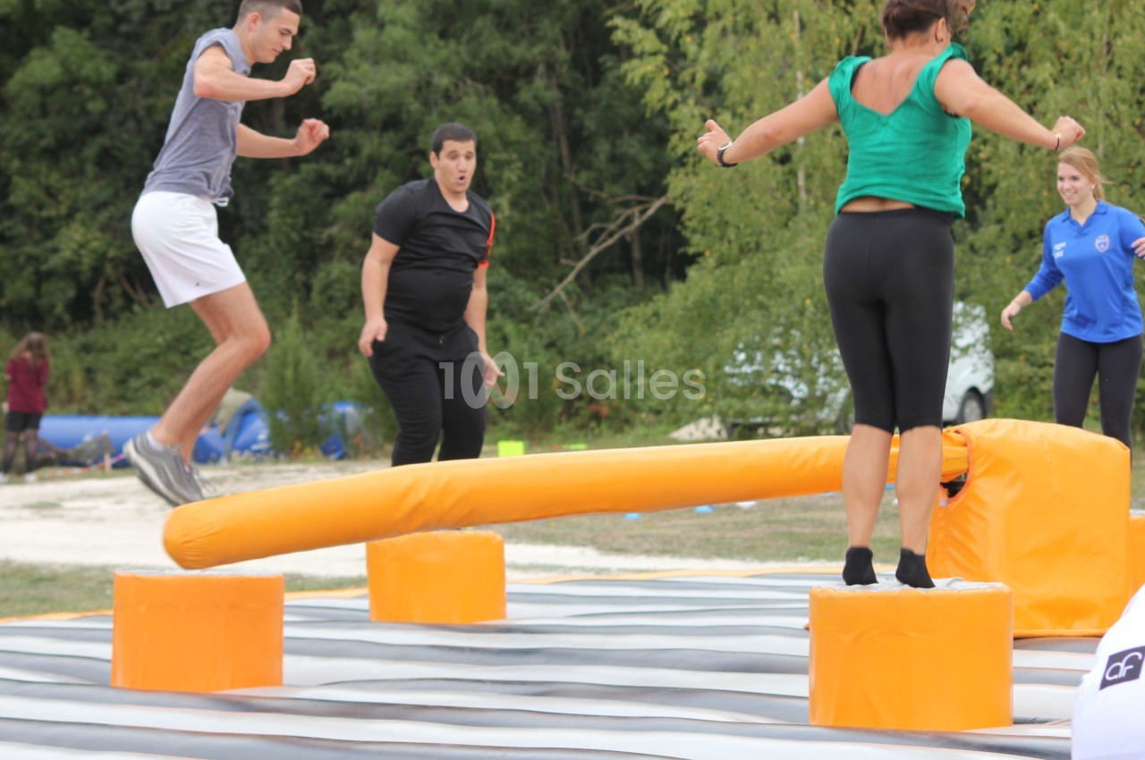 Des personnes participent à un jeu d'équilibre sur une structure gonflable avec une barre rotative.