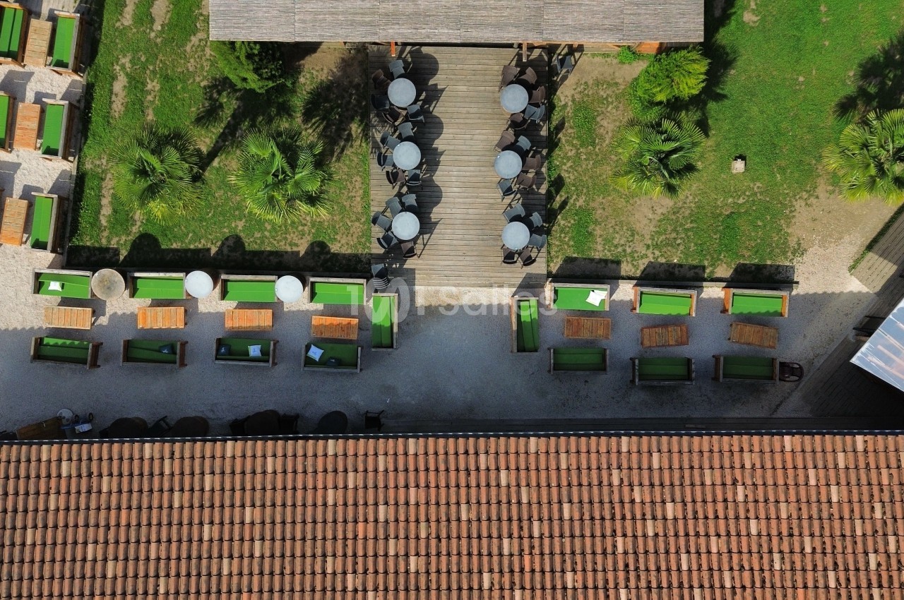 Vue aérienne d'une terrasse avec tables et chaises disposées autour d'allées en bois, entourée de verdure.