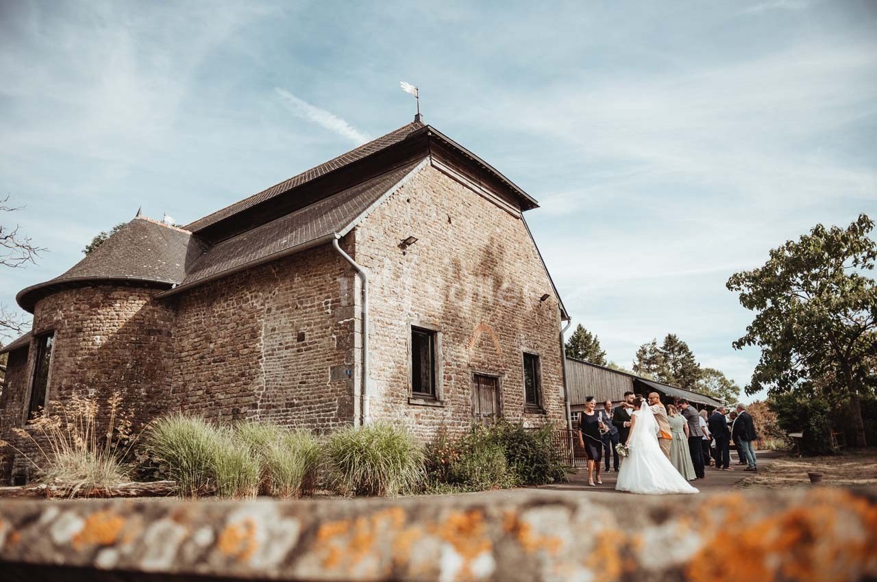 Un couple de mariés pose avec des invités devant un bâtiment en pierre dans un cadre champêtre.