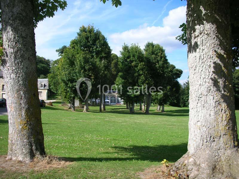 Pelouse verdoyante entourée d'arbres avec un bâtiment en arrière-plan sous un ciel bleu.