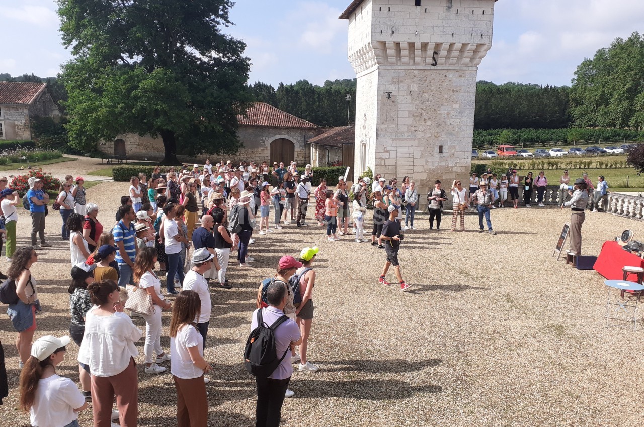 Groupe de personnes rassemblées en plein air devant une tour en pierre dans un cadre rural.