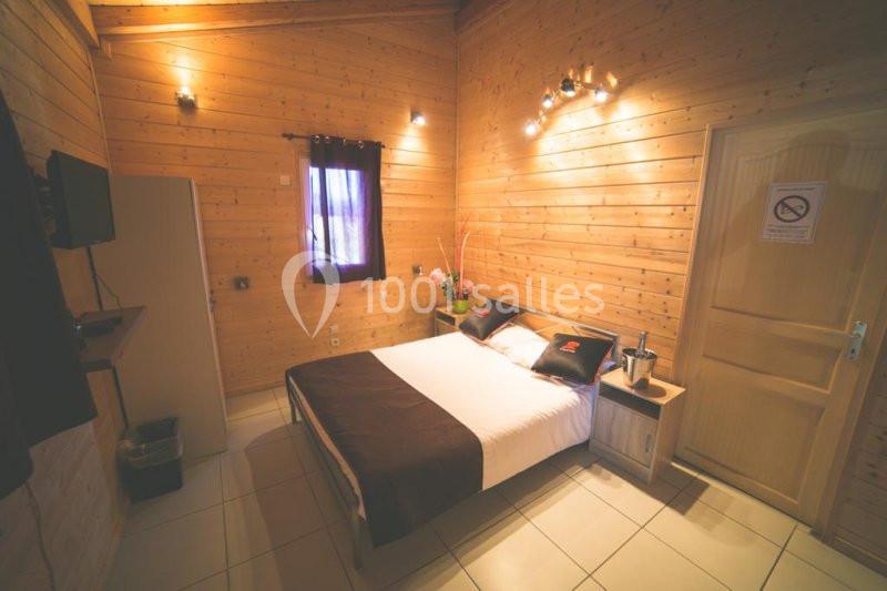 Chambre en bois avec un lit double, une fenêtre, un éclairage mural et une porte fermée.