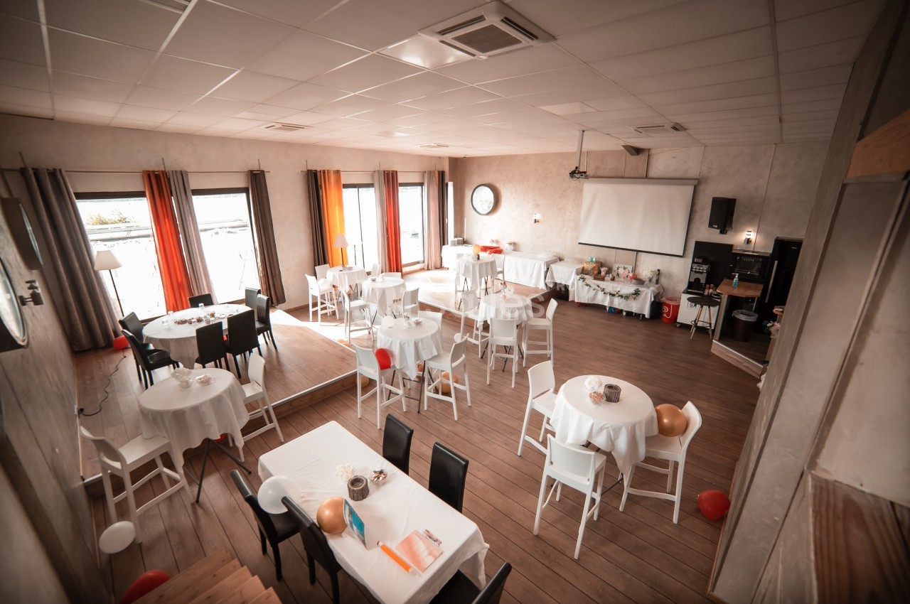 Salle de réception lumineuse avec tables rondes et rectangulaires dressées, décorée pour un événement.