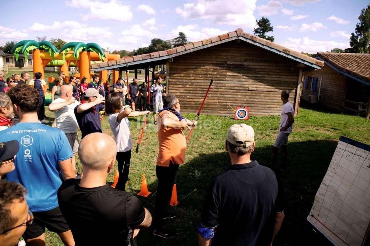 Des personnes participent à une activité de tir à l'arc en plein air, encadrées par un animateur devant une cible.