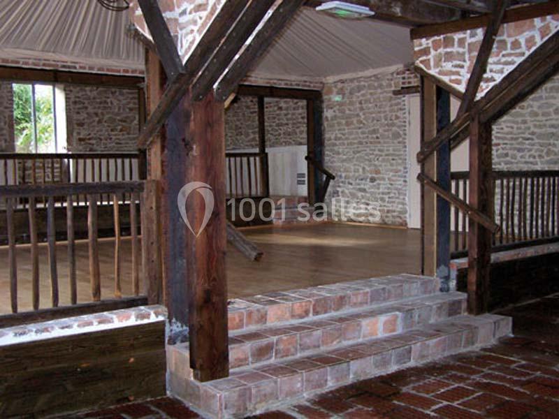 Salle intérieure avec murs en pierre, poutres en bois apparentes, sol en briques et parquet, éclairée par une fenêtre.