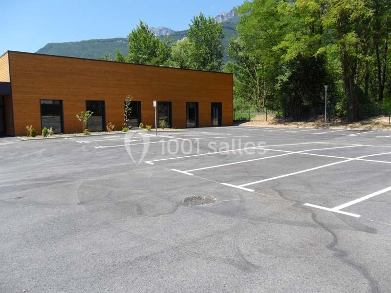 Parking vide avec marquages au sol, situé devant un bâtiment en bois entouré d'arbres et de montagnes.