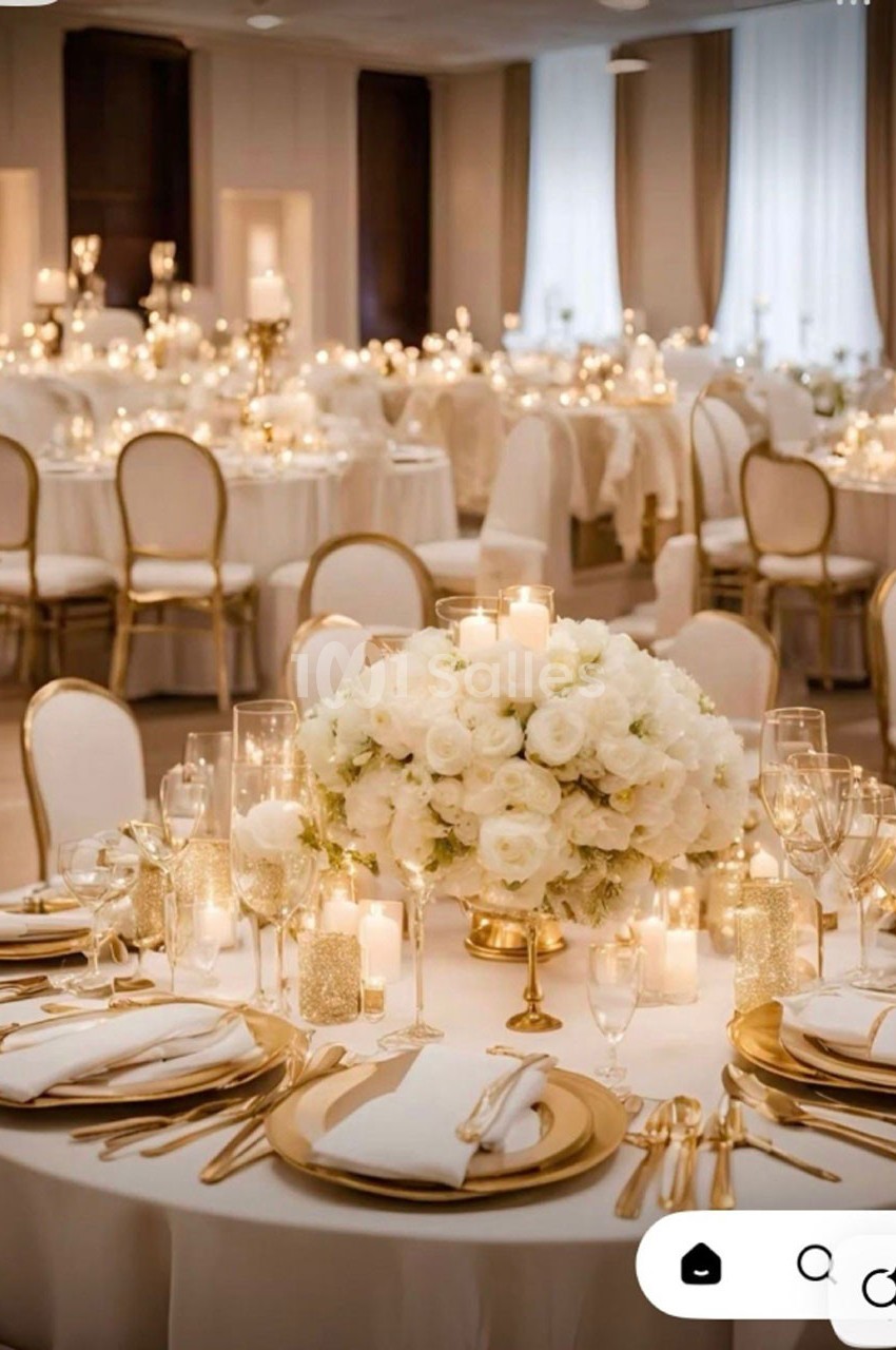 Salle de réception élégante avec tables décorées de fleurs blanches, bougies et vaisselle raffinée.