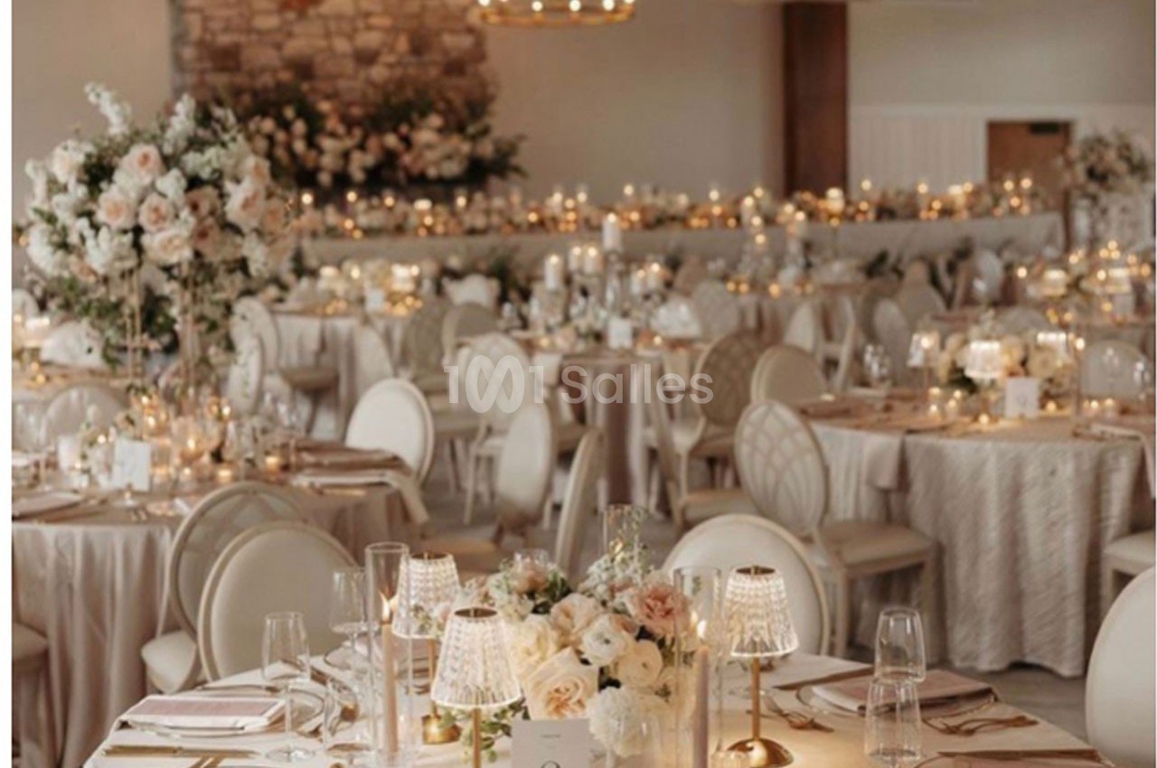Salle de réception élégante décorée de fleurs blanches, bougies et tables dressées pour un événement formel.