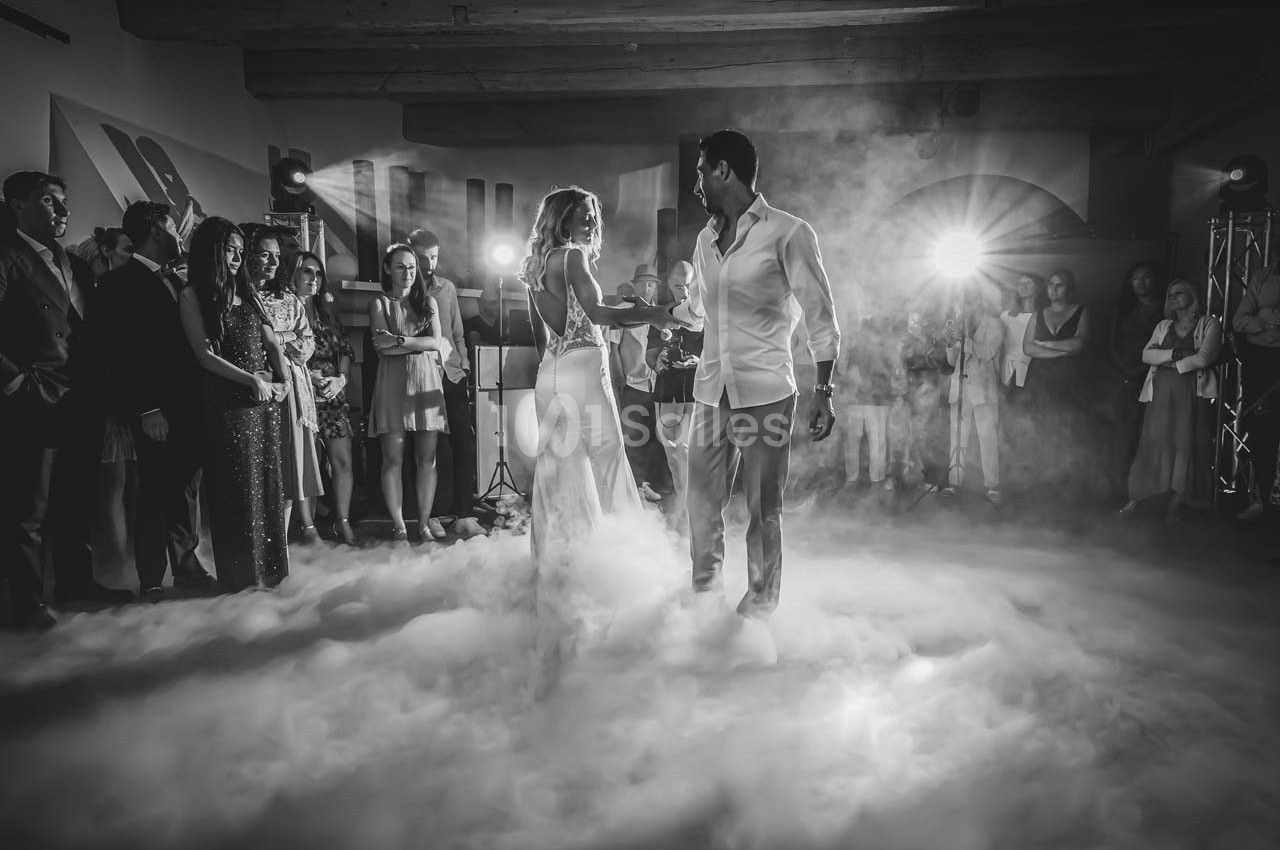 Un couple danse au milieu d'une piste enveloppée de fumée, entouré d'invités dans une ambiance festive.
