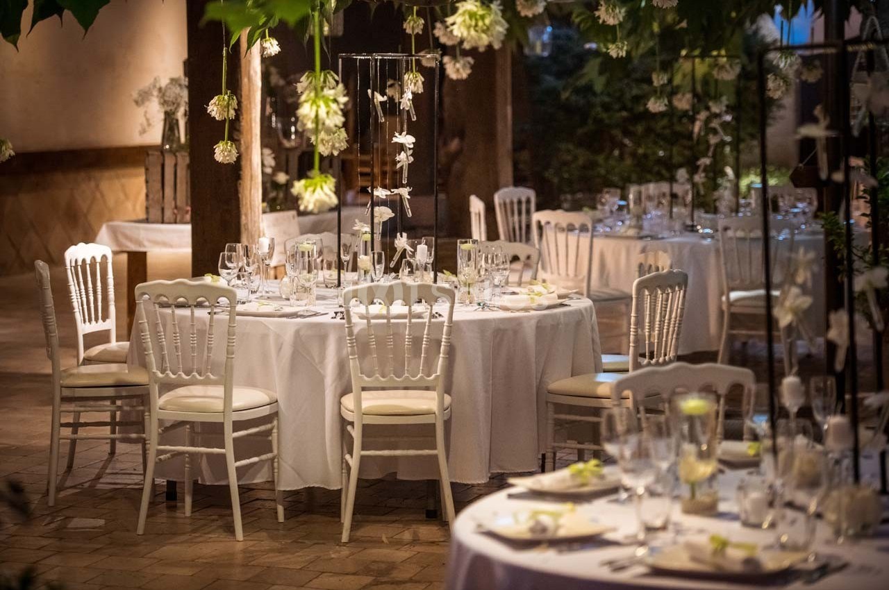 Salle de réception décorée avec des tables rondes, nappes blanches, chaises élégantes et éclairage tamisé.