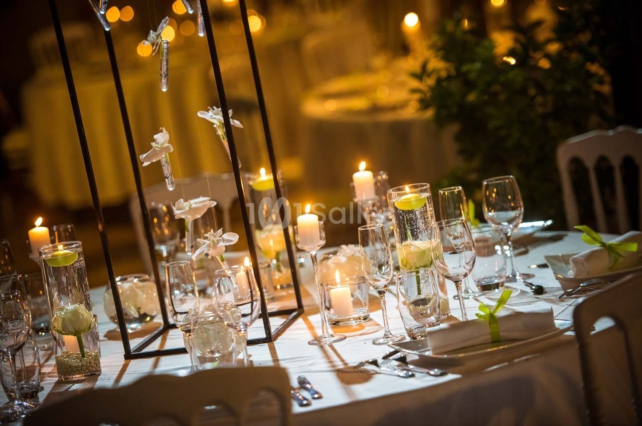 Table élégamment dressée avec bougies, verres, serviettes pliées et décorations florales dans une ambiance tamisée.