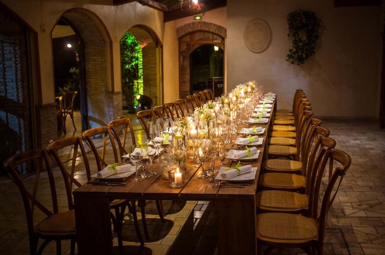 Grande table en bois décorée de bougies et de serviettes blanches, entourée de chaises dans une salle éclairée…