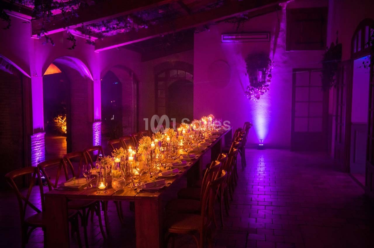 Table décorée avec des bougies et des verres dans une salle tamisée éclairée par des lumières violettes.