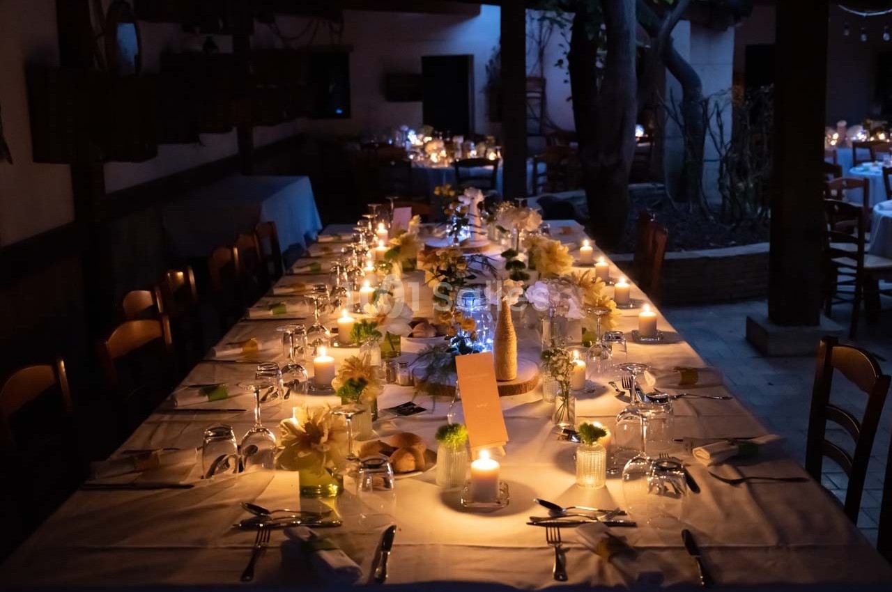 Grande table dressée pour un dîner, éclairée par des bougies, avec des fleurs et des couverts disposés soigneusement.