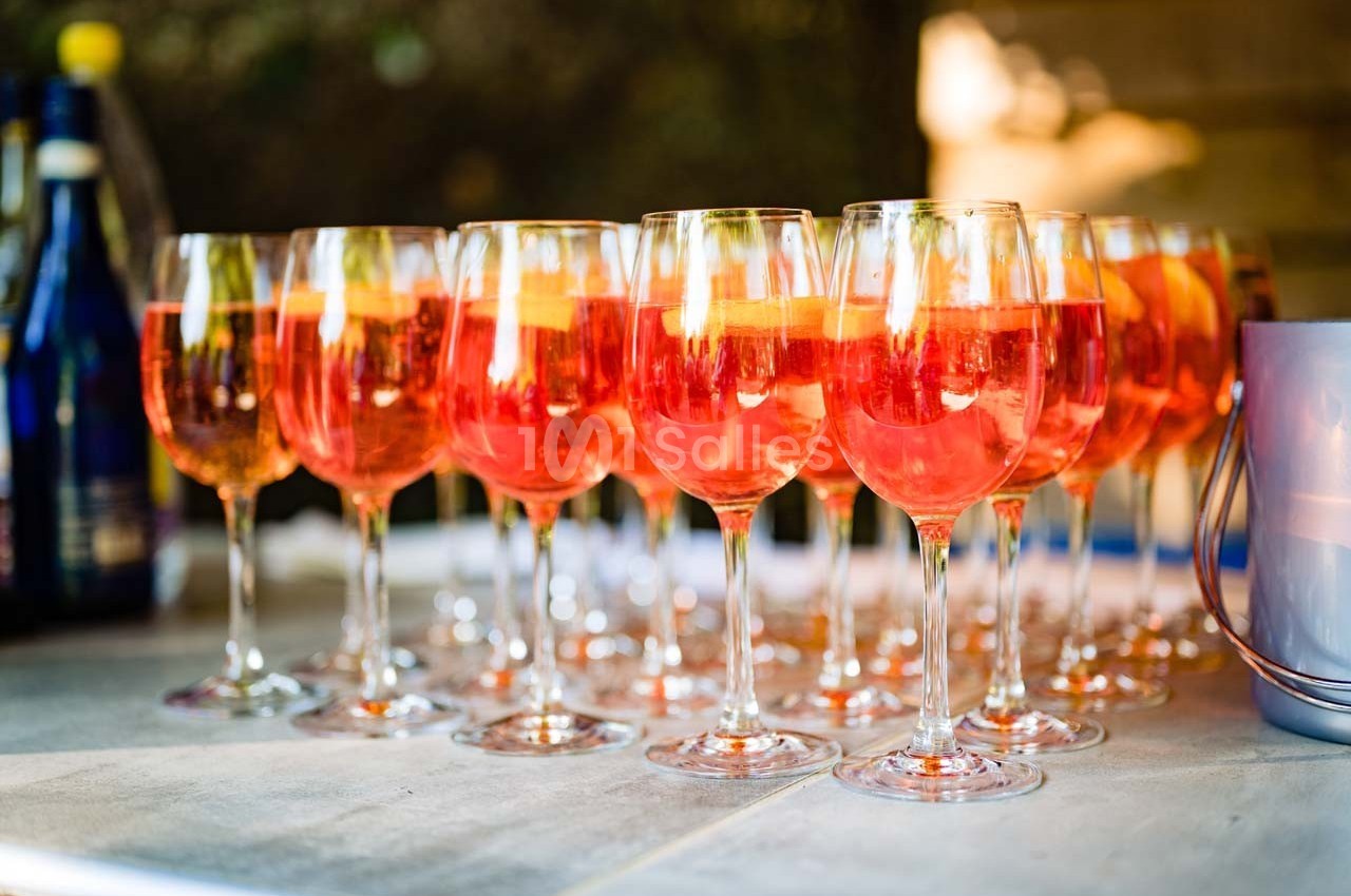 Verres de cocktail orange garnis de tranches d'orange, alignés sur une table en extérieur.