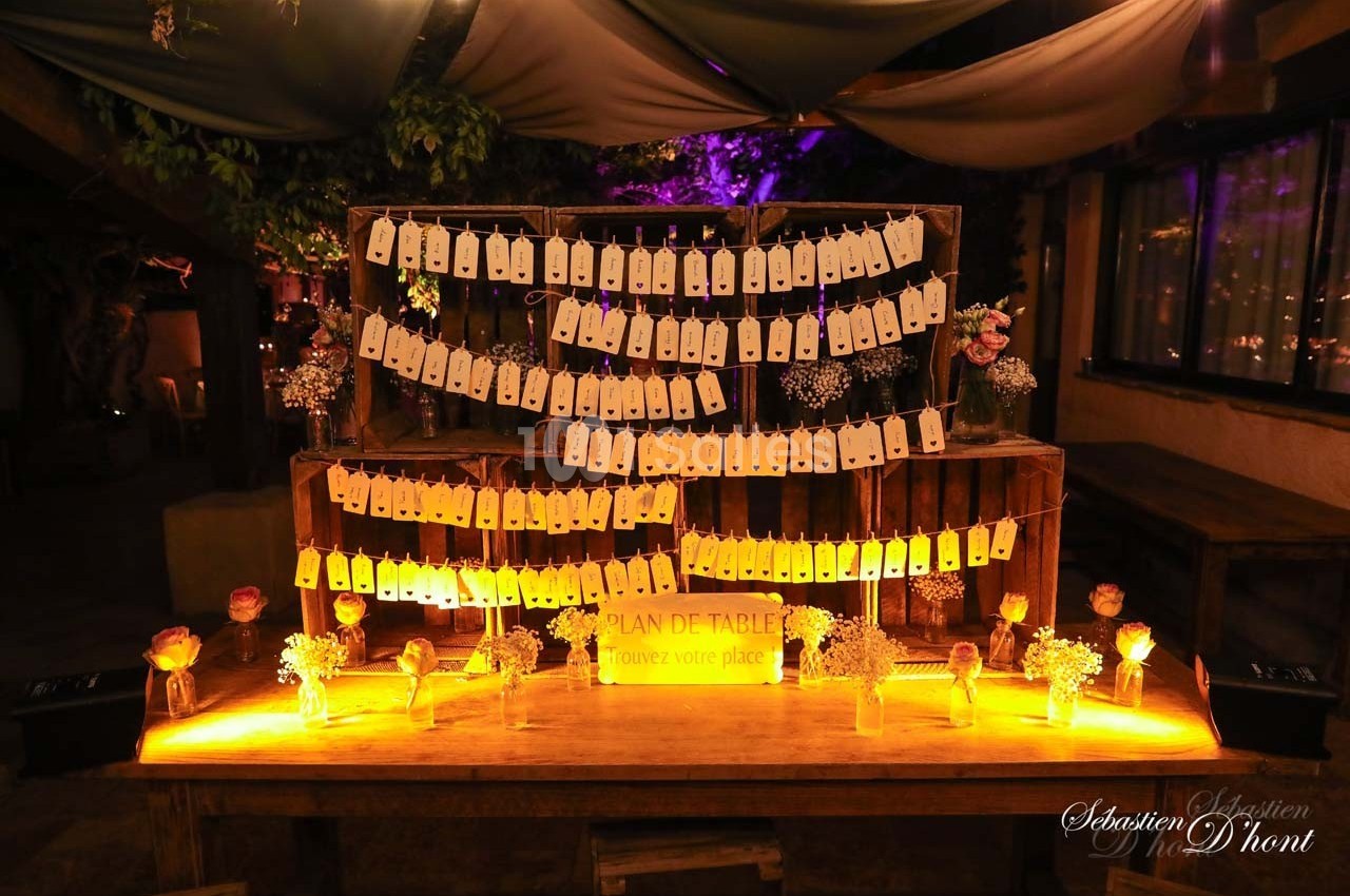 Plan de table lumineux avec étiquettes suspendues, entouré de décorations florales dans une ambiance tamisée.
