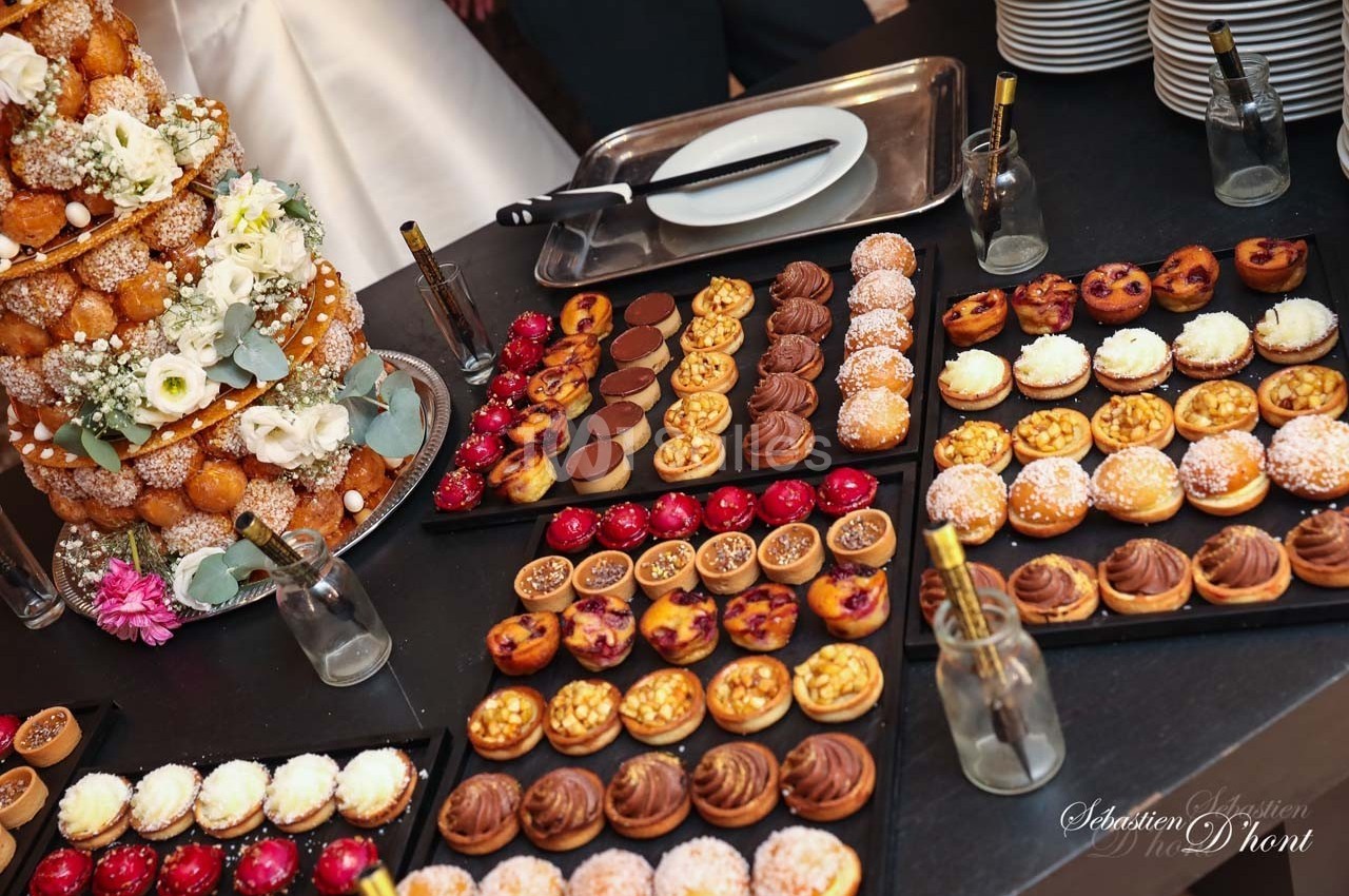 Plateau de desserts variés avec un croquembouche décoré de fleurs en arrière-plan sur une table de réception.