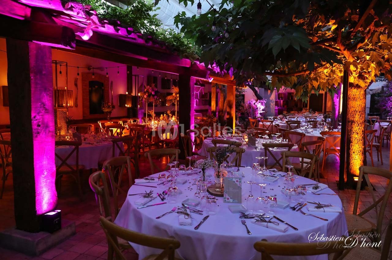 Salle de réception décorée avec des tables rondes dressées, éclairage coloré et ambiance chaleureuse en soirée.