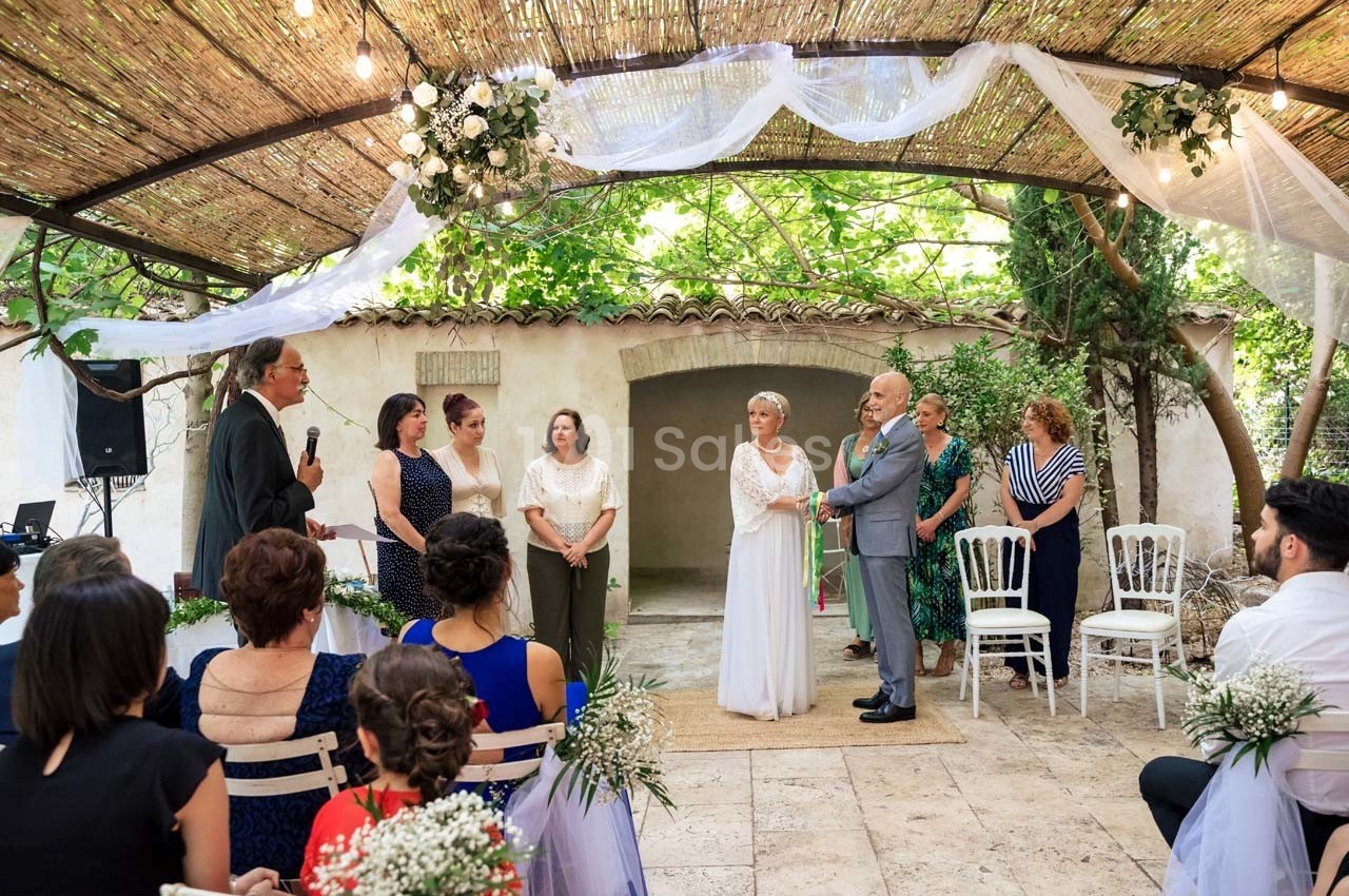 Un couple échange ses vœux lors d'une cérémonie de mariage en extérieur sous une pergola décorée.