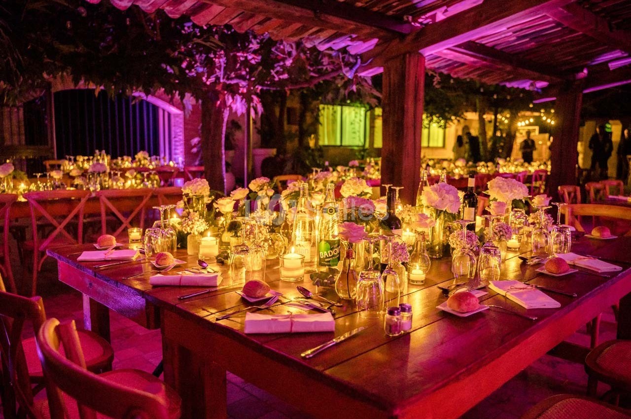 Tables en bois décorées de bougies, fleurs et vaisselle, éclairées par une lumière tamisée dans un cadre extérieur nocturne.