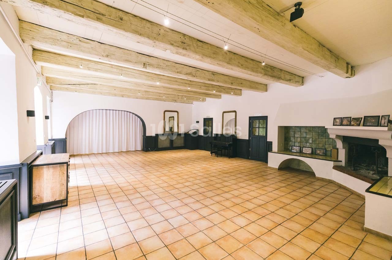 Salle lumineuse avec poutres apparentes, carrelage au sol, cheminée et mobilier en bois sombre.
