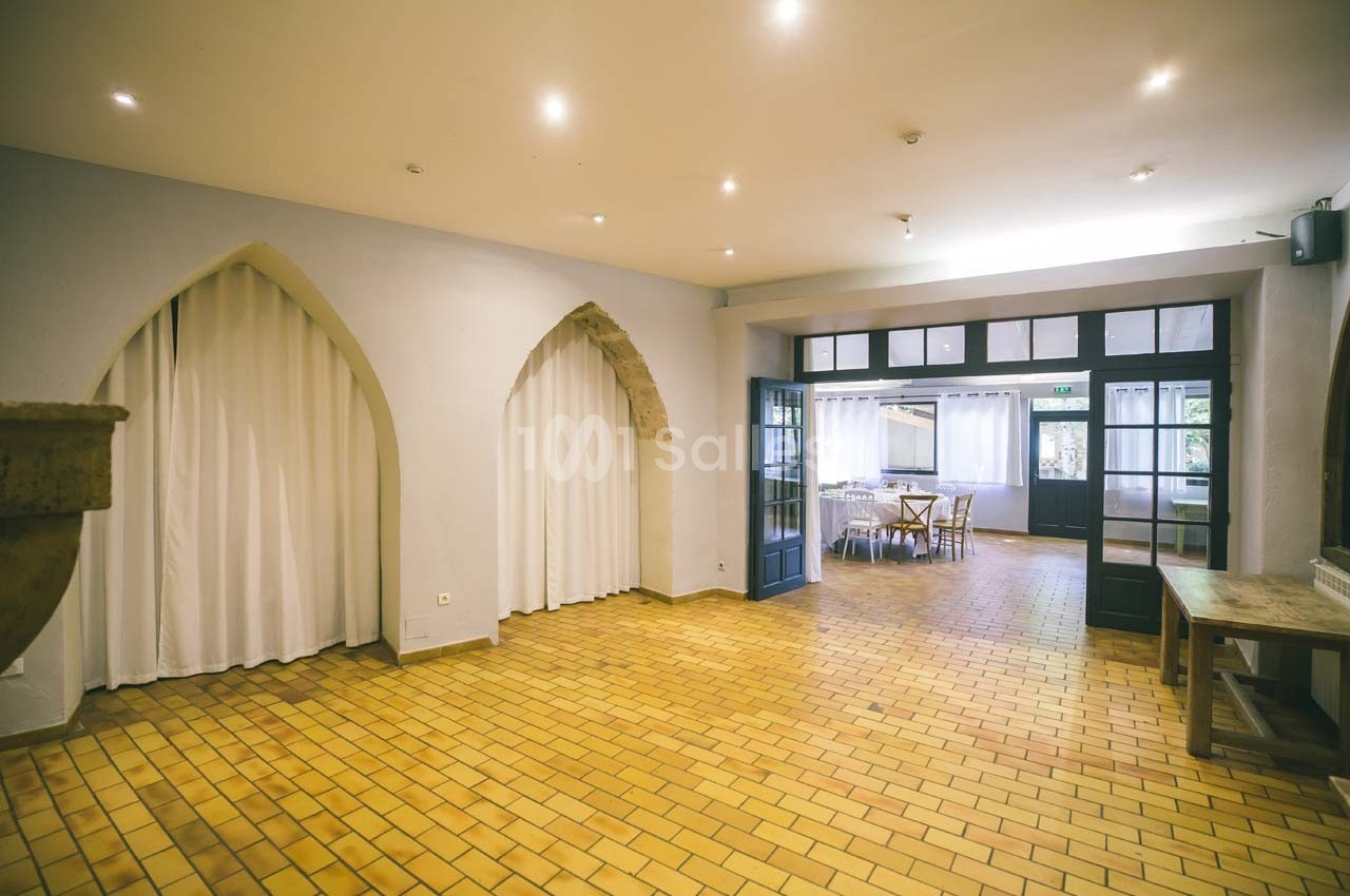Salle lumineuse avec carrelage jaune, murs clairs, grandes ouvertures vitrées et rideaux blancs.