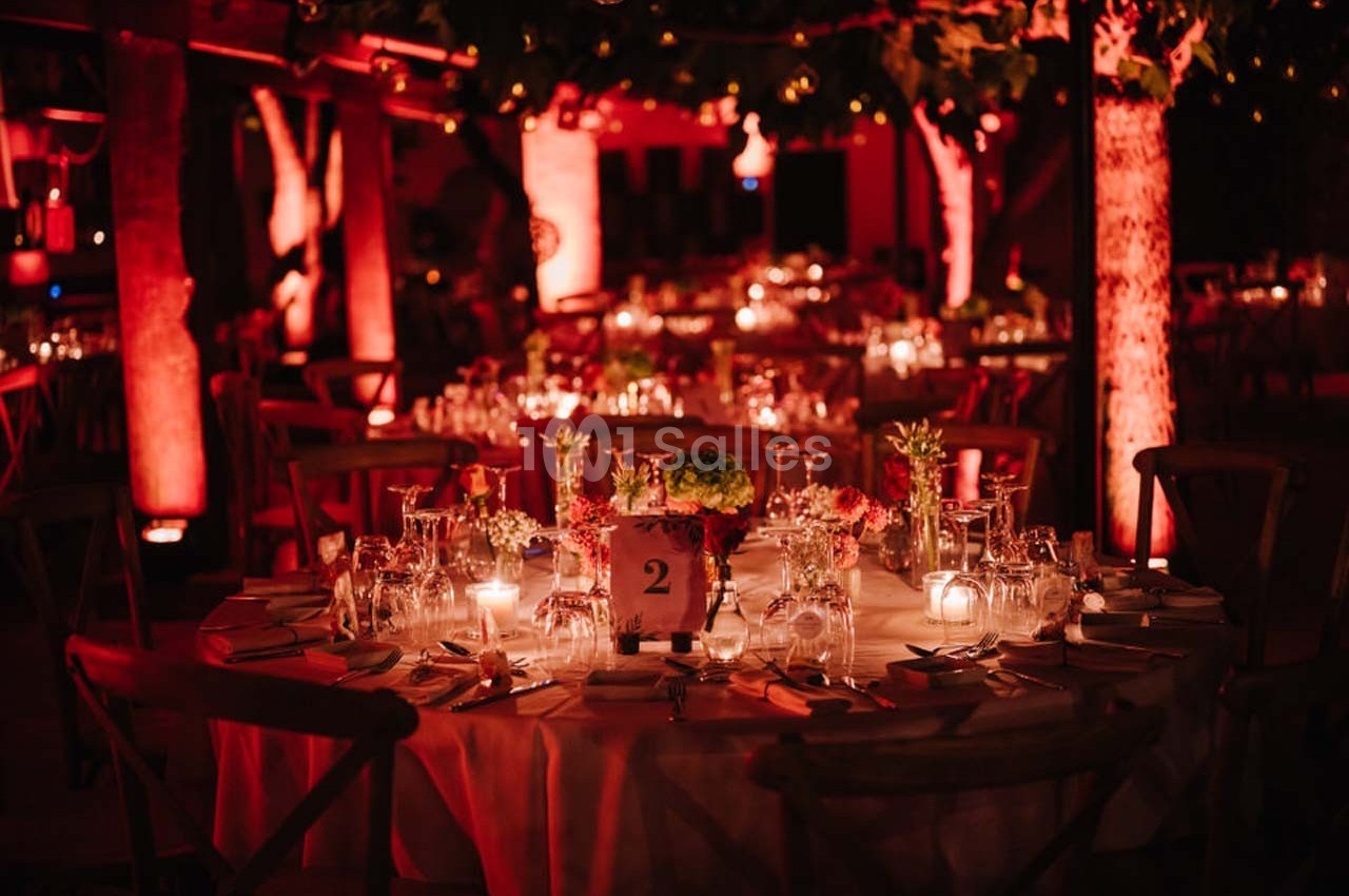 Tables rondes décorées avec des bougies et des fleurs, éclairées par une lumière rouge dans un cadre extérieur nocturne.