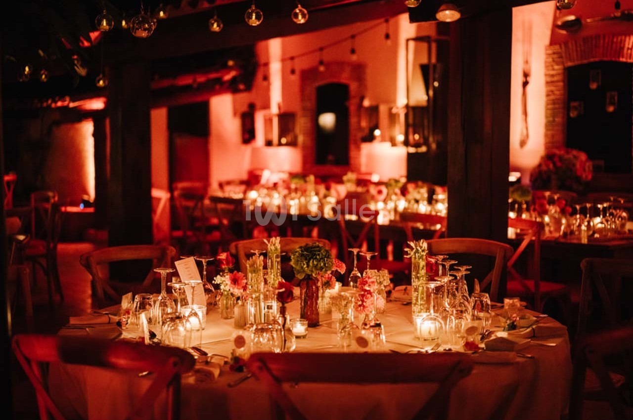 Salle de réception chaleureusement éclairée avec des tables décorées de fleurs, bougies et vaisselle élégante.