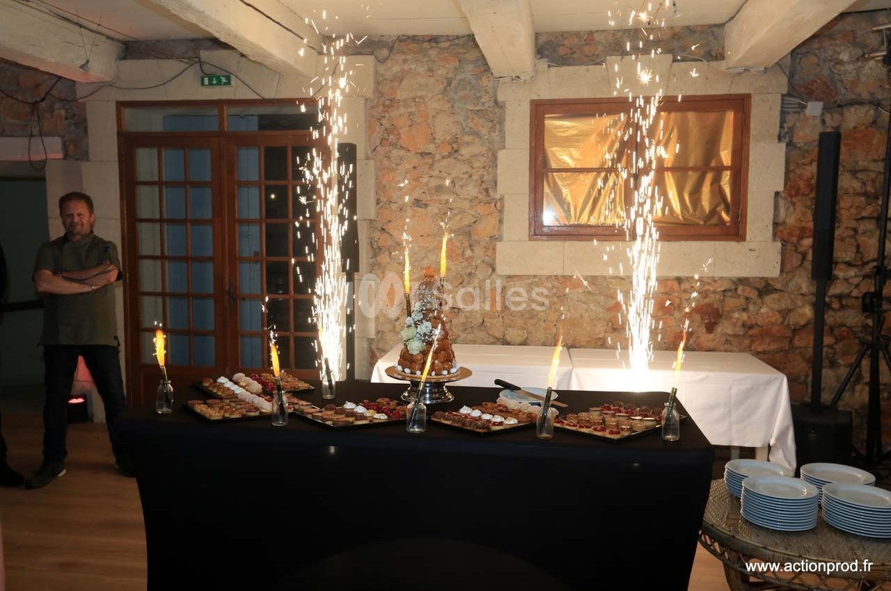 Table de desserts avec un croquembouche central, entourée de fontaines lumineuses dans une salle en pierre.