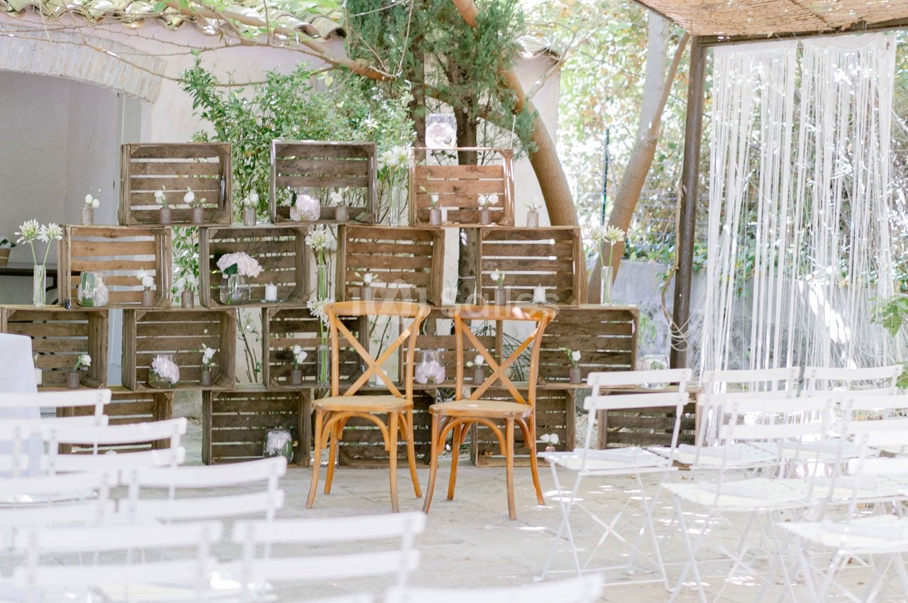 Deux chaises en bois devant un décor rustique composé de caisses en bois et de fleurs, dans un espace extérieur.