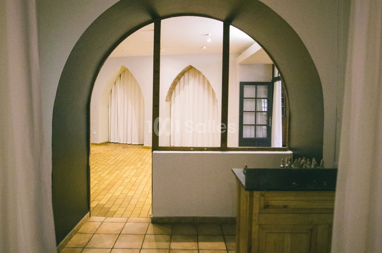 Vue d'un intérieur avec une arche, des rideaux blancs et un sol en carreaux de terre cuite.