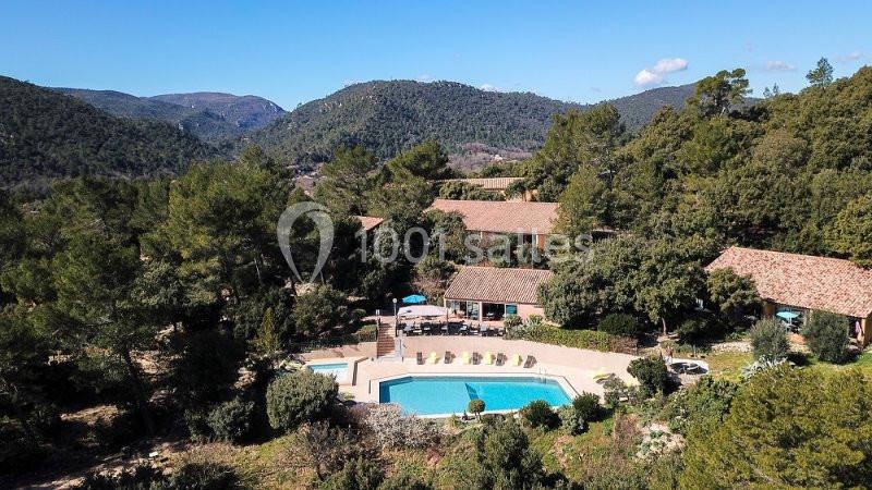 Vue aérienne d'un domaine avec piscine entouré de collines boisées et de bâtiments aux toits en tuiles.