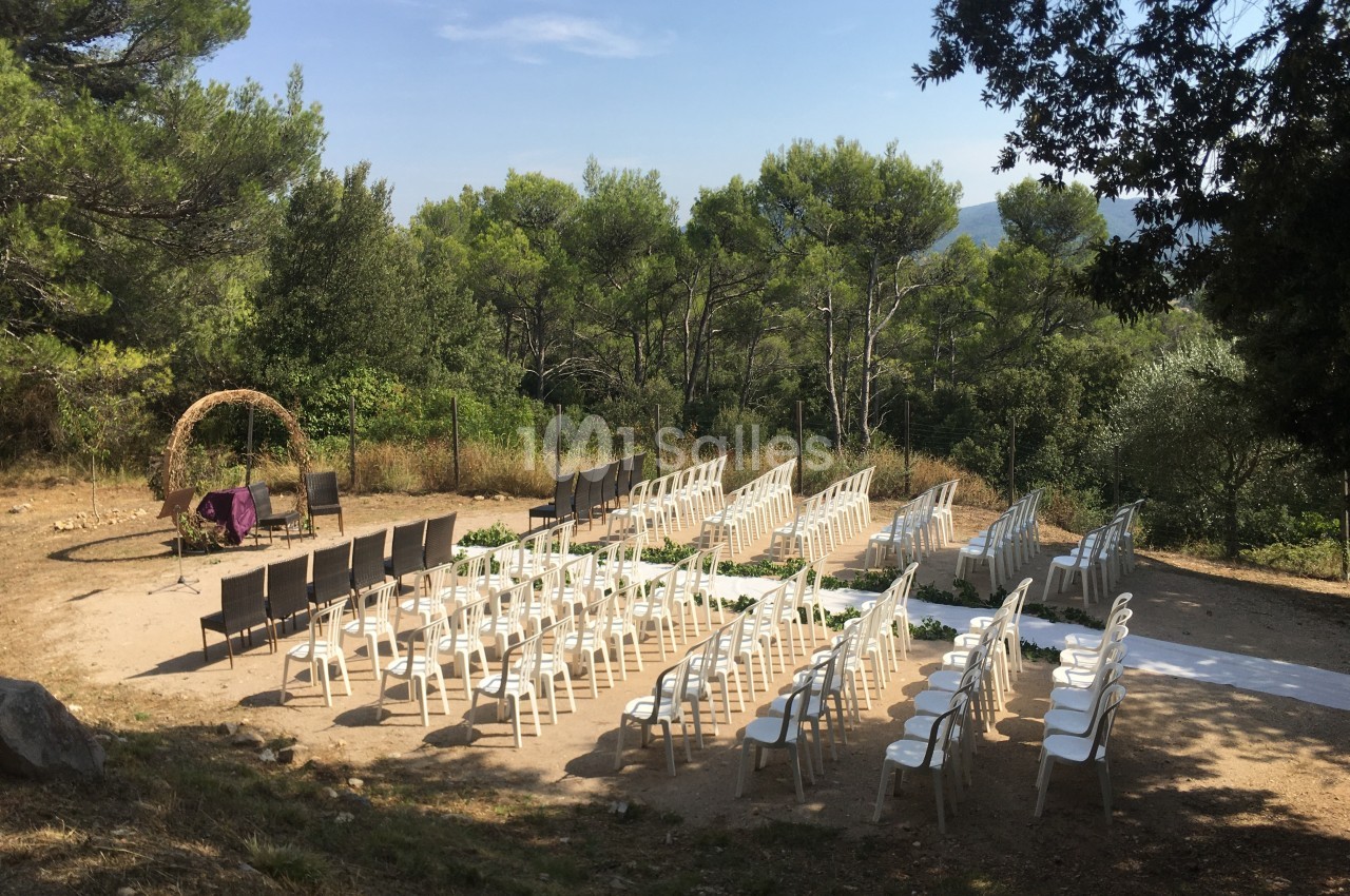 Chaises disposées en extérieur sous des arbres, formant une allée centrale, avec une arche décorative en arrière-plan.